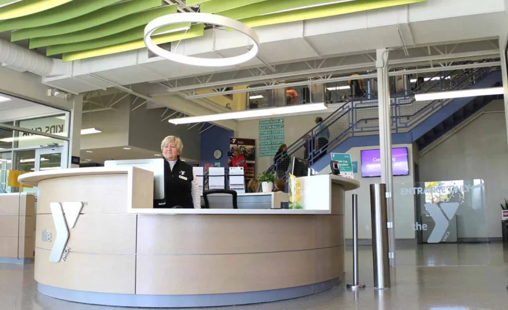 A woman stands behind the YMCA desk at the front entrance waiting to greet you at YMCA of the North Shore