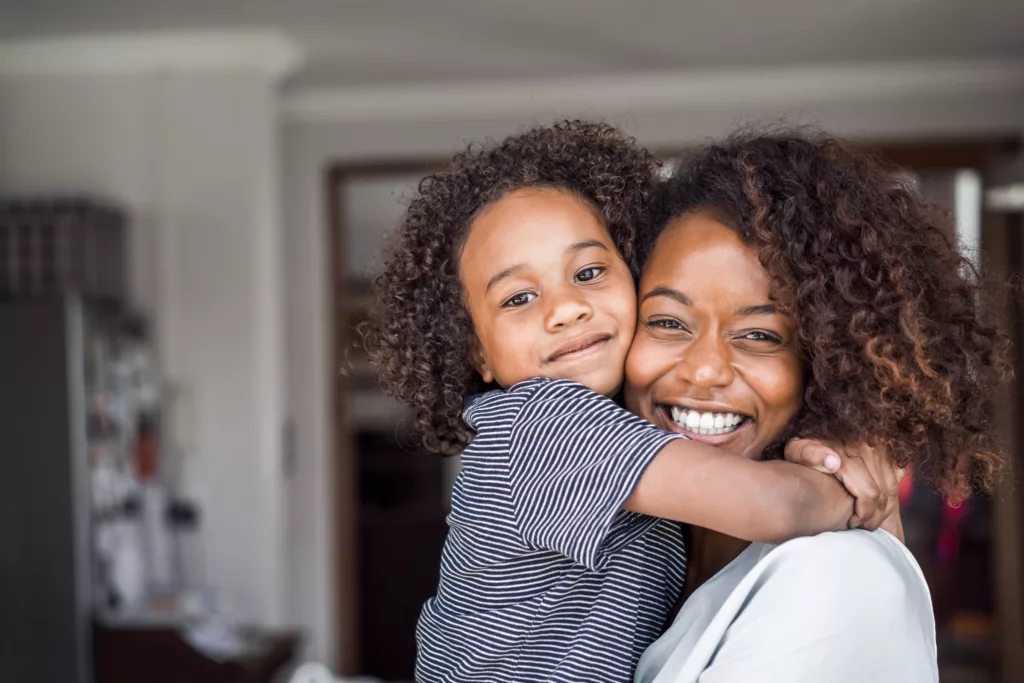 A photo of mother and daughter embracing. Portrait of happy woman and girl with curly and frizzy hair. They are in casuals at home.