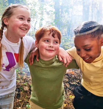 Three YMCA students embrace while enjoying summer camp in the woods near the YMCA of the North Shore