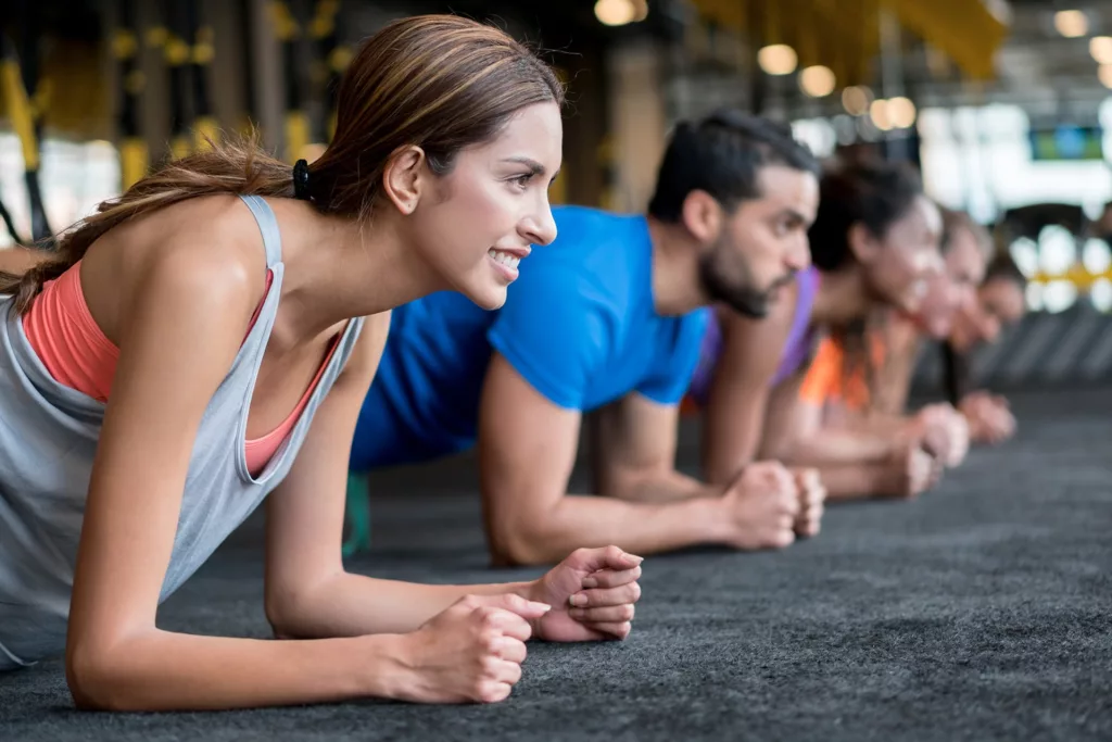 YMCA community members lay in a line doing forearm planks on a black mat