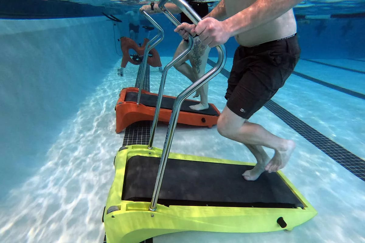 An underwater perspective of a man and a women running on treadmills with other liquid gym equipment in the background.