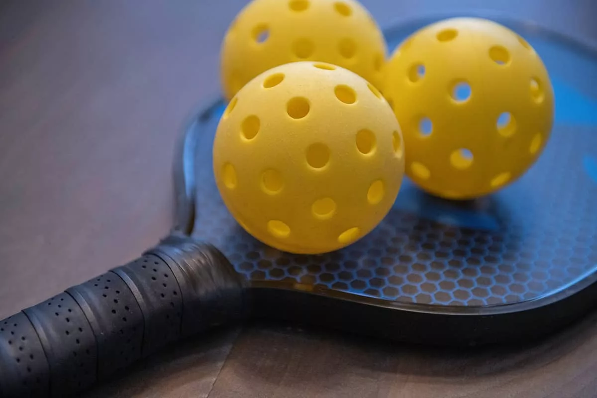 Three yellow pickleballs sit atop a black pickleball racquet