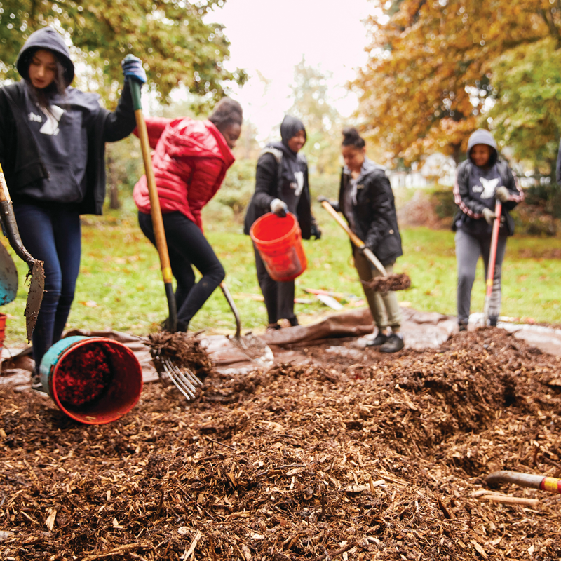 A group of youth in YMCA hoodies move mulch around at a Go Green Event in 2019
