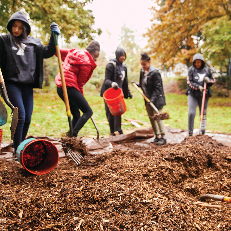 2019_10-19_GoGreenEvent_2118_01_CMYK A group of youth in YMCA hoodies move mulch around at a Go Green Event in 2019