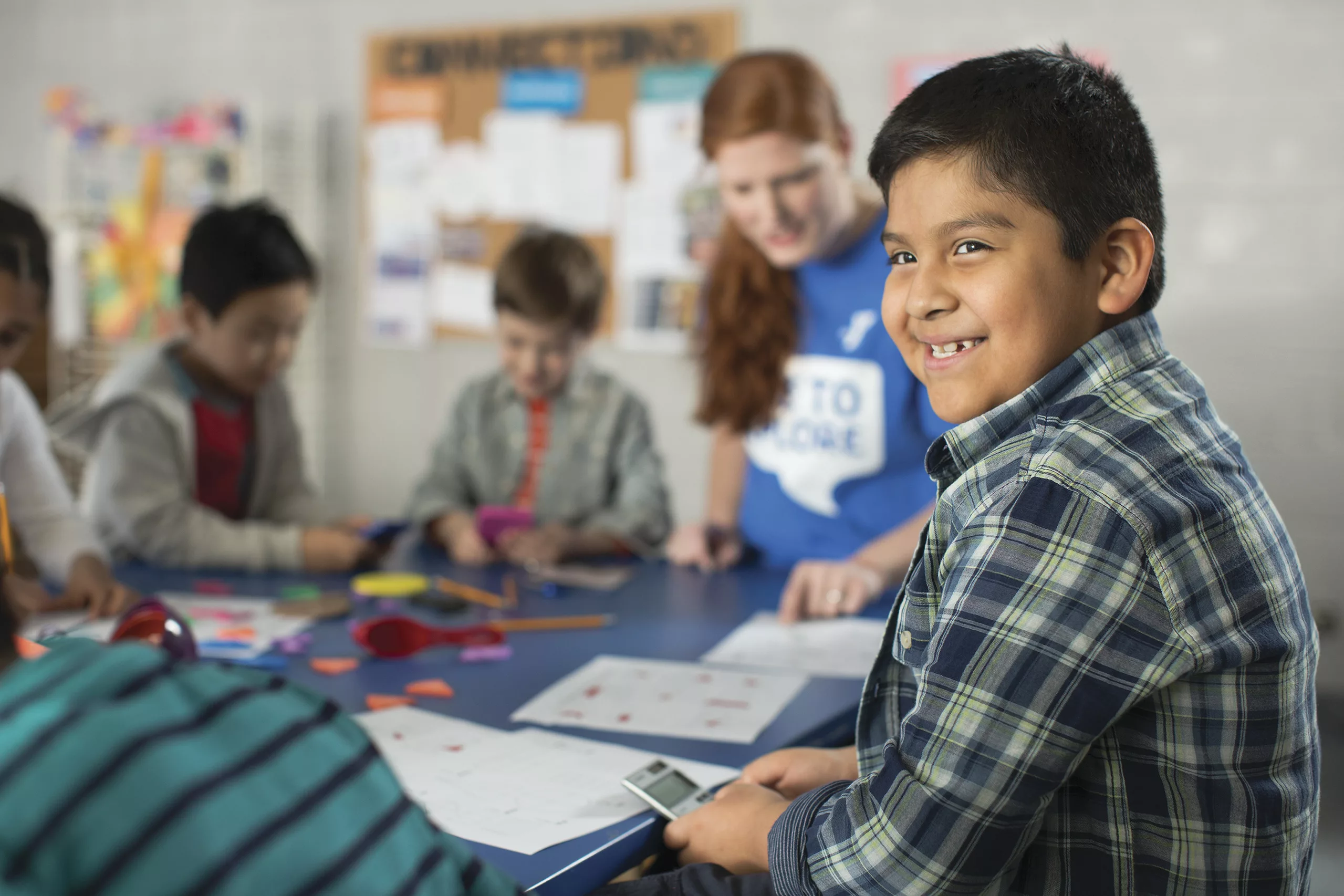 A young boy smiles as the camera as he folds a calculator in his hands during the YMCA of the North Shore afterschool program