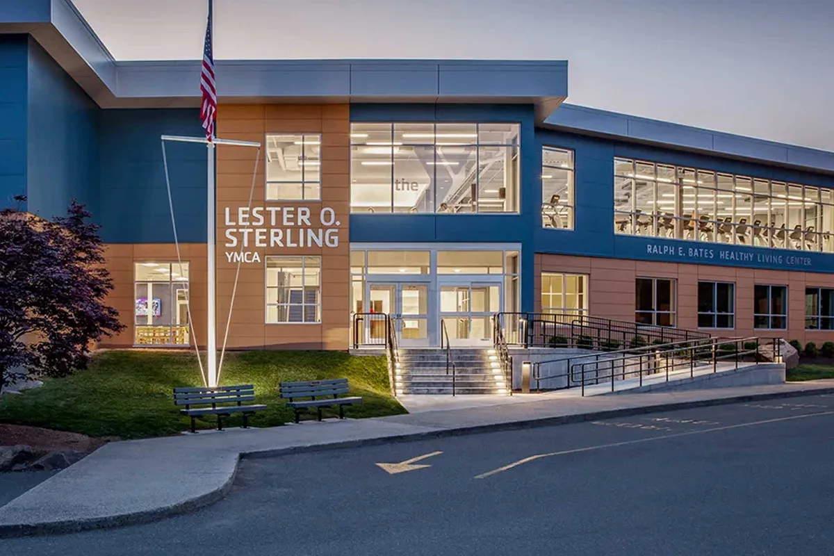 An exterior image of the blue and brick Lester O Sterling YMCA and Ralph E. Bates Healthy Living Center just before dusk