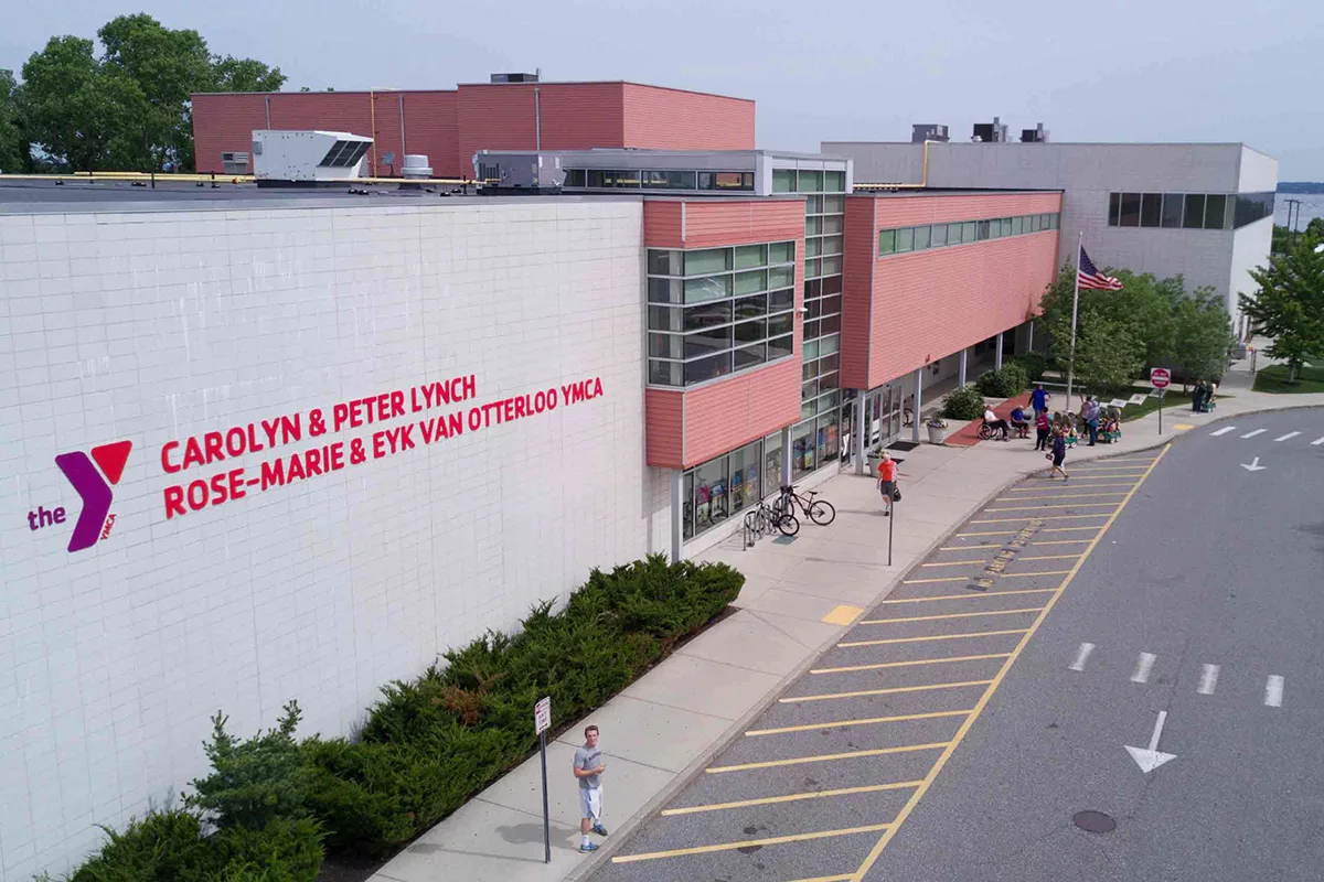 An aerial photo of the gray and red brick Carolyn & Peter Lynch Rose Marie & Eyk Van Otterloo YMCA with guests walking around the exterior.