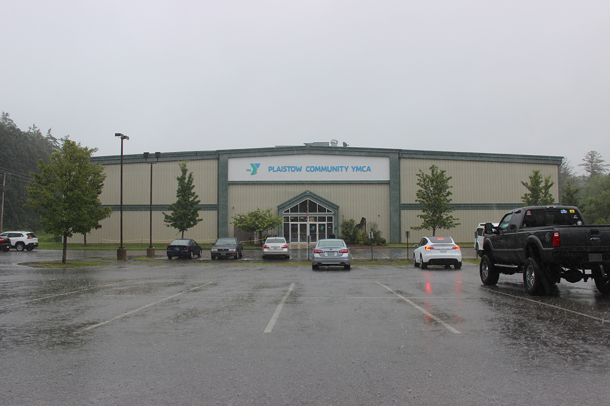 An exterior view of the green and beiege Plaistow Community YMCA from the parking lot during a light rain