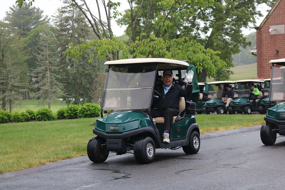 A gentlemen dressed to play golf waves from his car on an overcast day at the YMCA Regional Golf Tournament