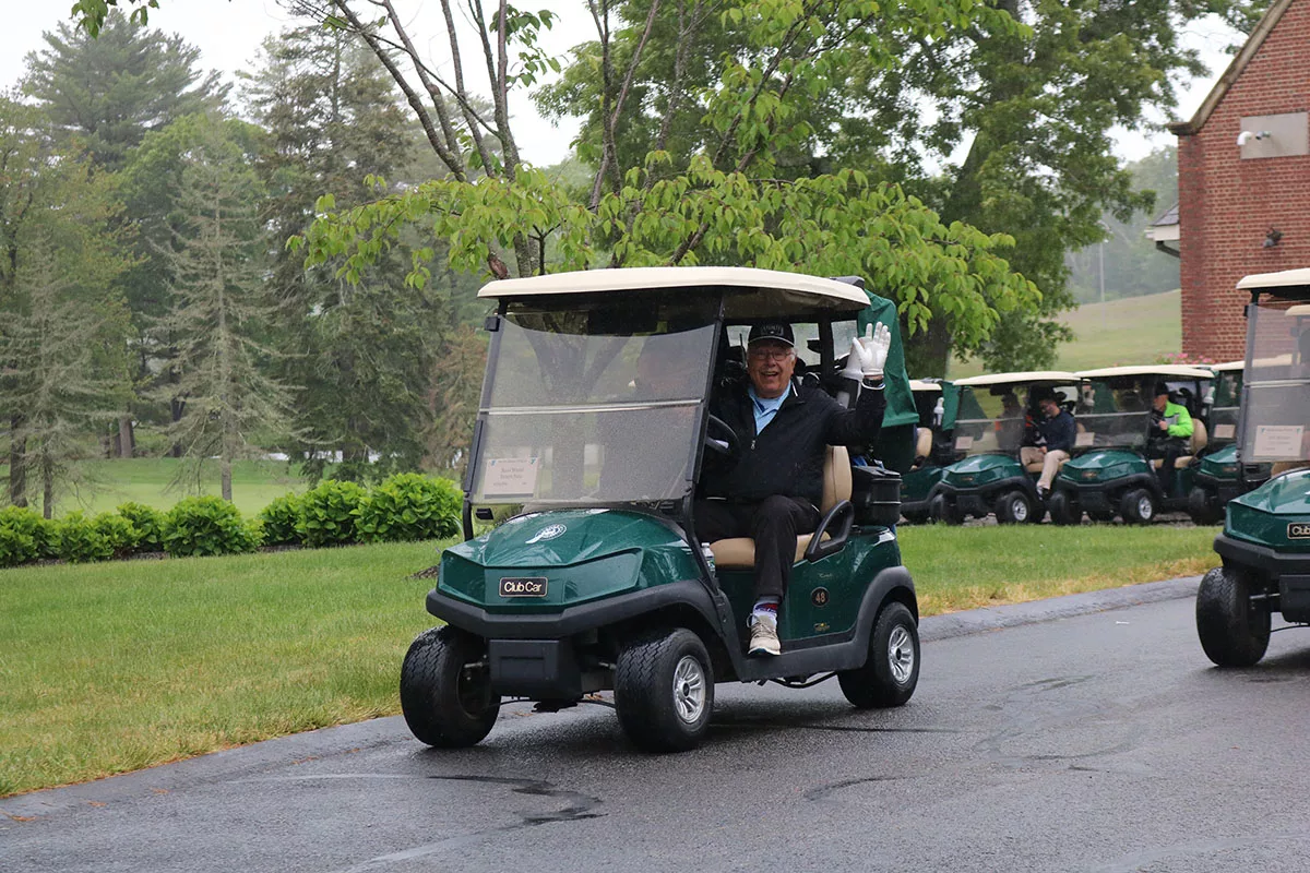 YMCA Regional Golf Tournament YMCA of the North Shore Ipswich Family YMCA_ A gentlemen dressed to play golf waves from his car on an overcast day at the YMCA Regional Golf Tournament